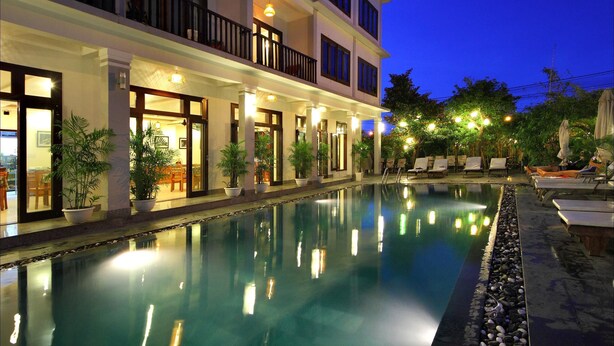 A nighttime view of a hotel with a swimming pool, outdoor seating, and well-lit balconies. - Sunshine Hoian Hotel (Da Nang)