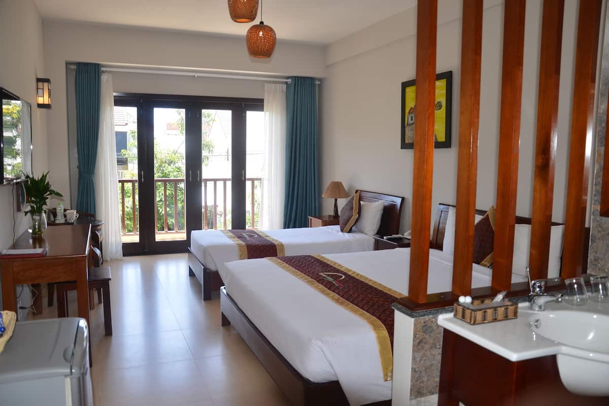 A hotel room with two beds, a dining table, a desk, a chair, a sink, and a balcony with curtains.