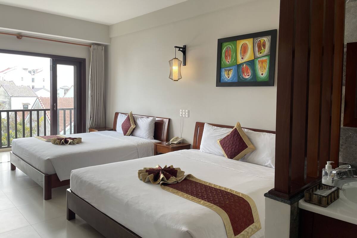 A hotel room with two beds, a balcony, a painting, and a bathroom with a sink and toiletries.