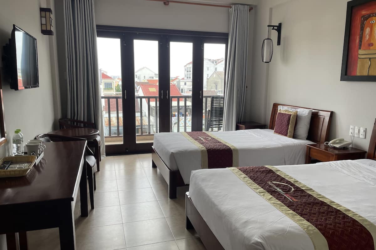A hotel room with two beds, a desk, a chair, a TV, and a balcony with curtains.