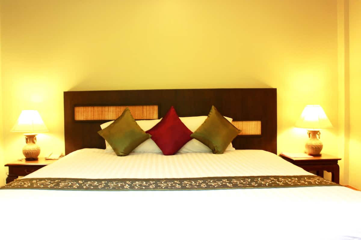 A bed with a wooden headboard, two bedside lamps, and three pillows.