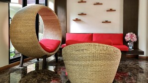 A modern lobby with a red sofa, two woven chairs, a marble floor, and decorative wall shelves. - Hua Hin White Sand (Hua Hin)