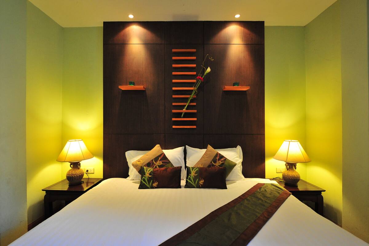 A hotel room with a large bed, two bedside lamps, and a wooden headboard with a vertical light strip.