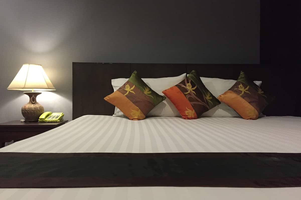 A neatly made bed with striped bedding, a bedside lamp, a telephone, and decorative pillows.