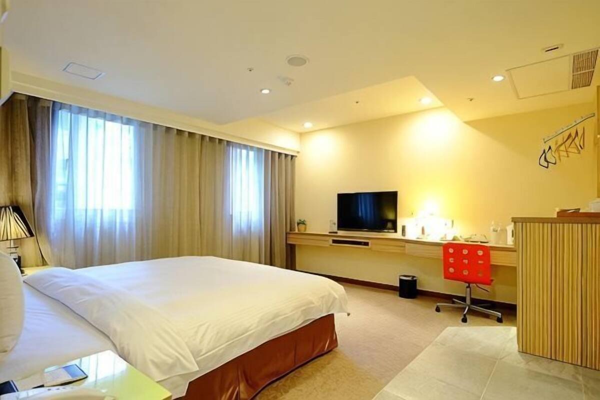 A hotel room with a large bed, a desk with a computer, a TV, and a bathroom area.