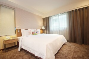 Een hotelkamer met een groot bed, een nachtkastje met een lamp, een telefoon en een raam met gordijnen.
