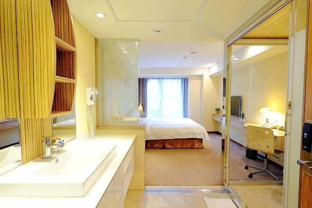A hotel room with a large mirror, a bed, a desk, and a television.
