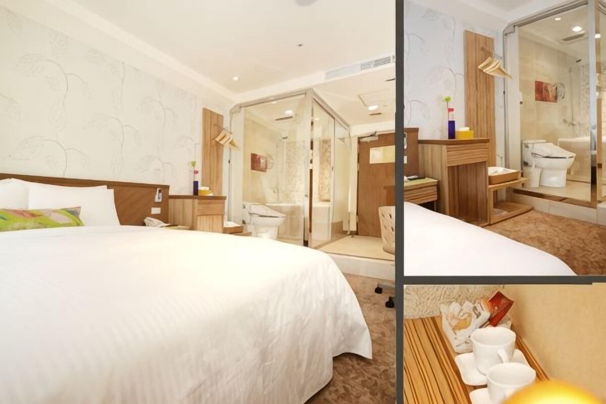 Hotelkamer met een groot bed, een badkamer met een douchecabine van glas en een zithoek met stoelen.