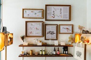 Una pared con carteles informativos enmarcados, un estante de madera con varios objetos, y una pequeña mesa con un florero y una vela.