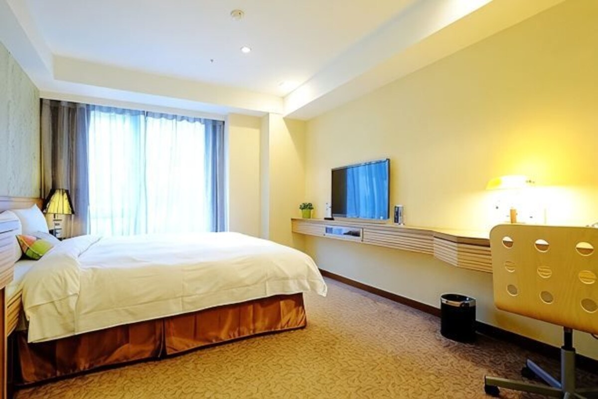 A hotel room with a bed, a desk, a chair, a television, and a window with curtains.
