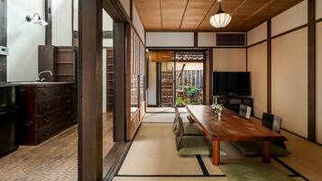 A traditional Japanese-style room with tatami flooring, a wooden dining table, and a television.