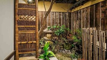 A traditional Japanese garden with a bamboo fence, a stone lantern, and a small pond.