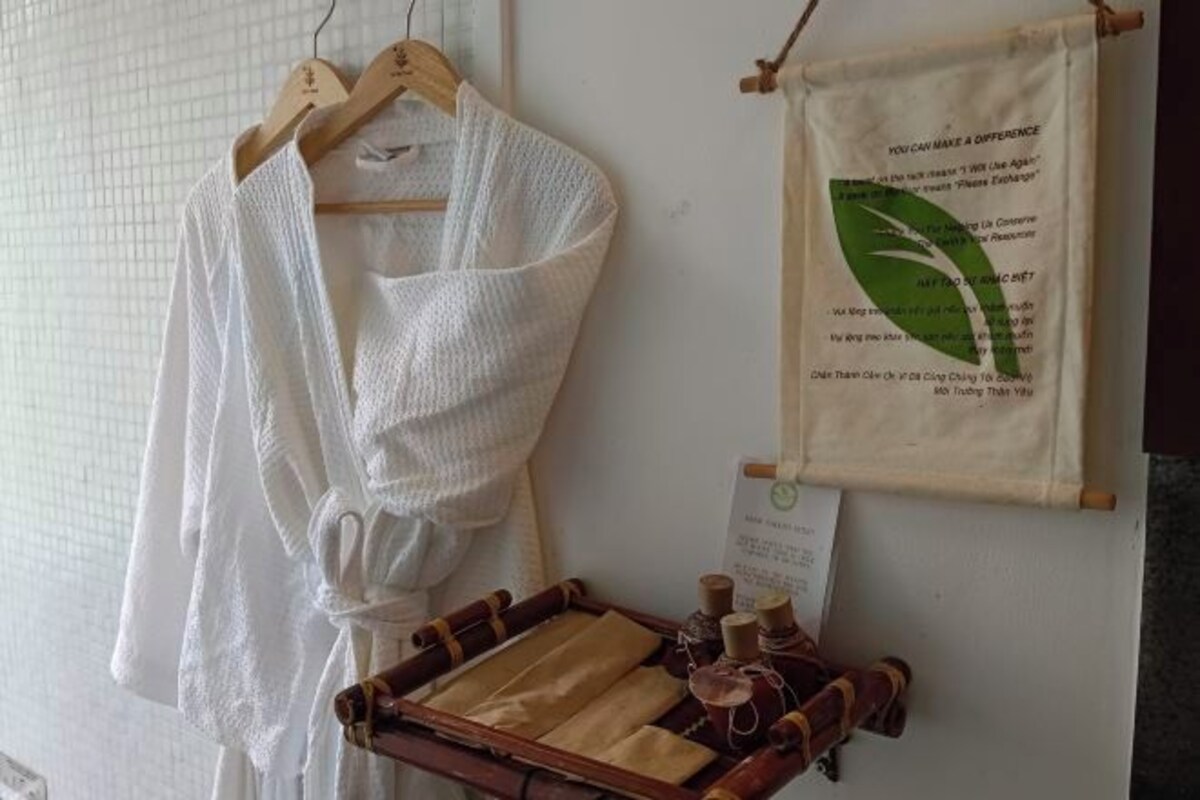 A white robe hanging on a wooden hanger, a bamboo tray with towels, and a sign with a green leaf and text.