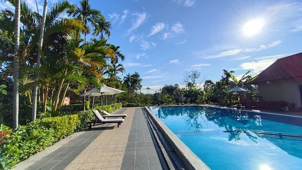 A swimming pool with lounge chairs and umbrellas, surrounded by palm trees and a clear sky. - Hue Riverside Boutique Resort & Spa (Hue)