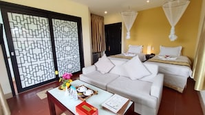 A hotel room with a sofa, two beds, a decorative screen, a table with a vase and water bottles, and a ceiling fan. - Hue Riverside Boutique Resort & Spa (Hue)