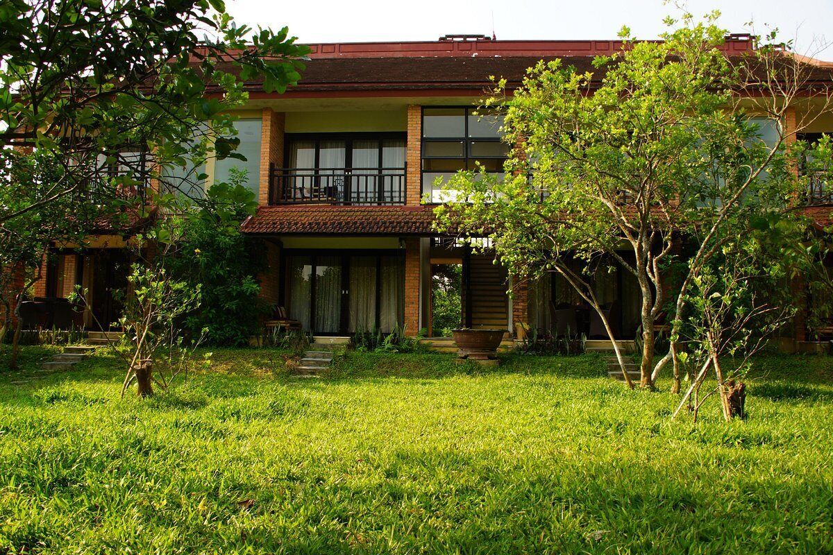 A two-story house with a balcony, surrounded by a well-maintained lawn and trees.