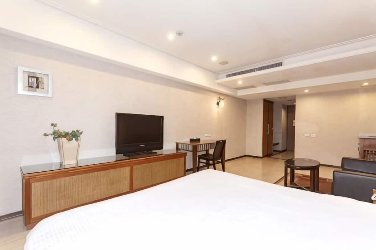 A hotel room with a bed, a television, a small dining table, and a seating area.