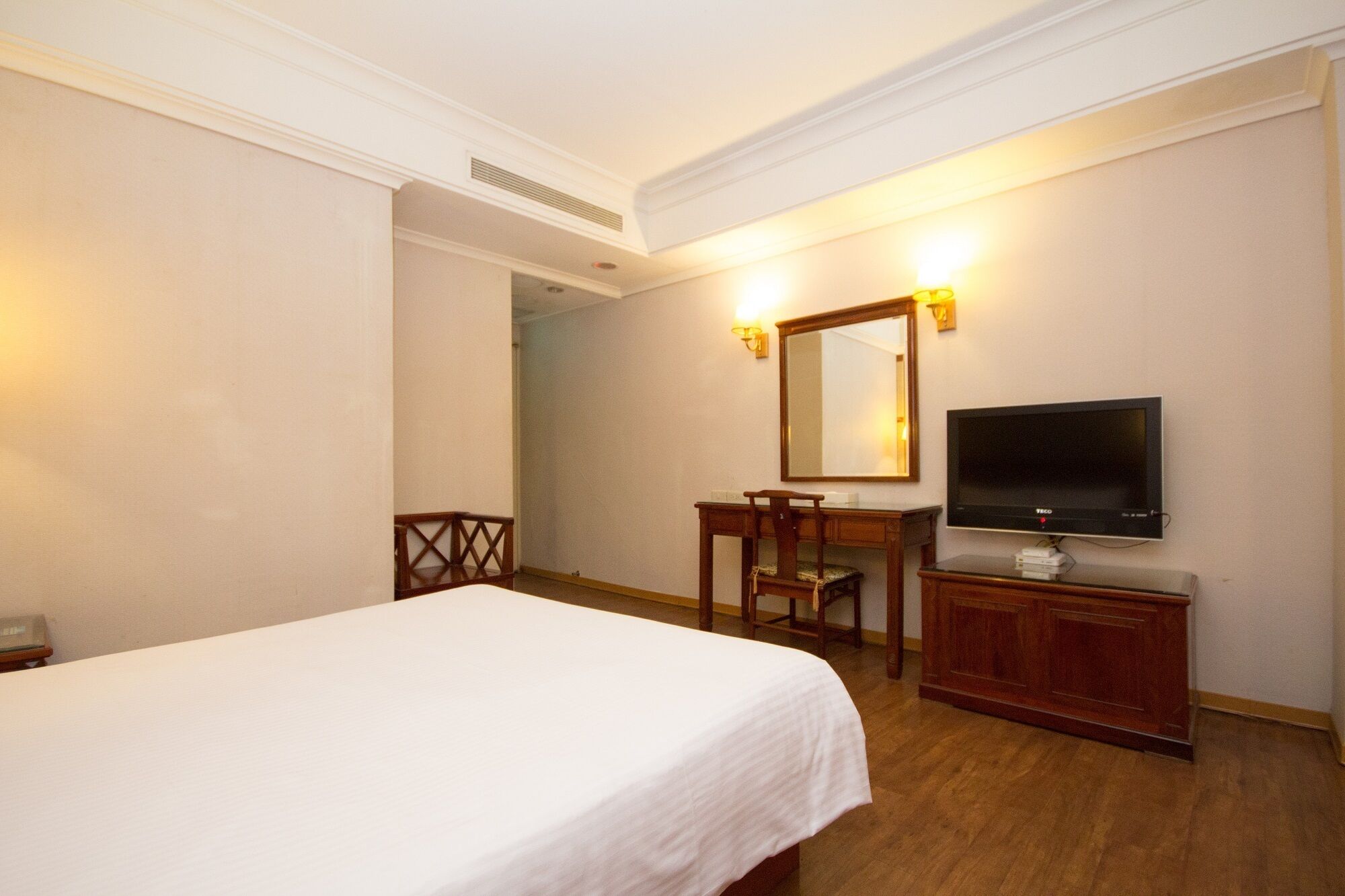 A hotel room with a bed, a desk with a chair, a television, and a mirror.