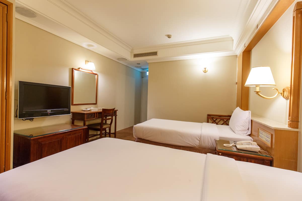 A hotel room with two beds, a desk, a television, and a lamp.
