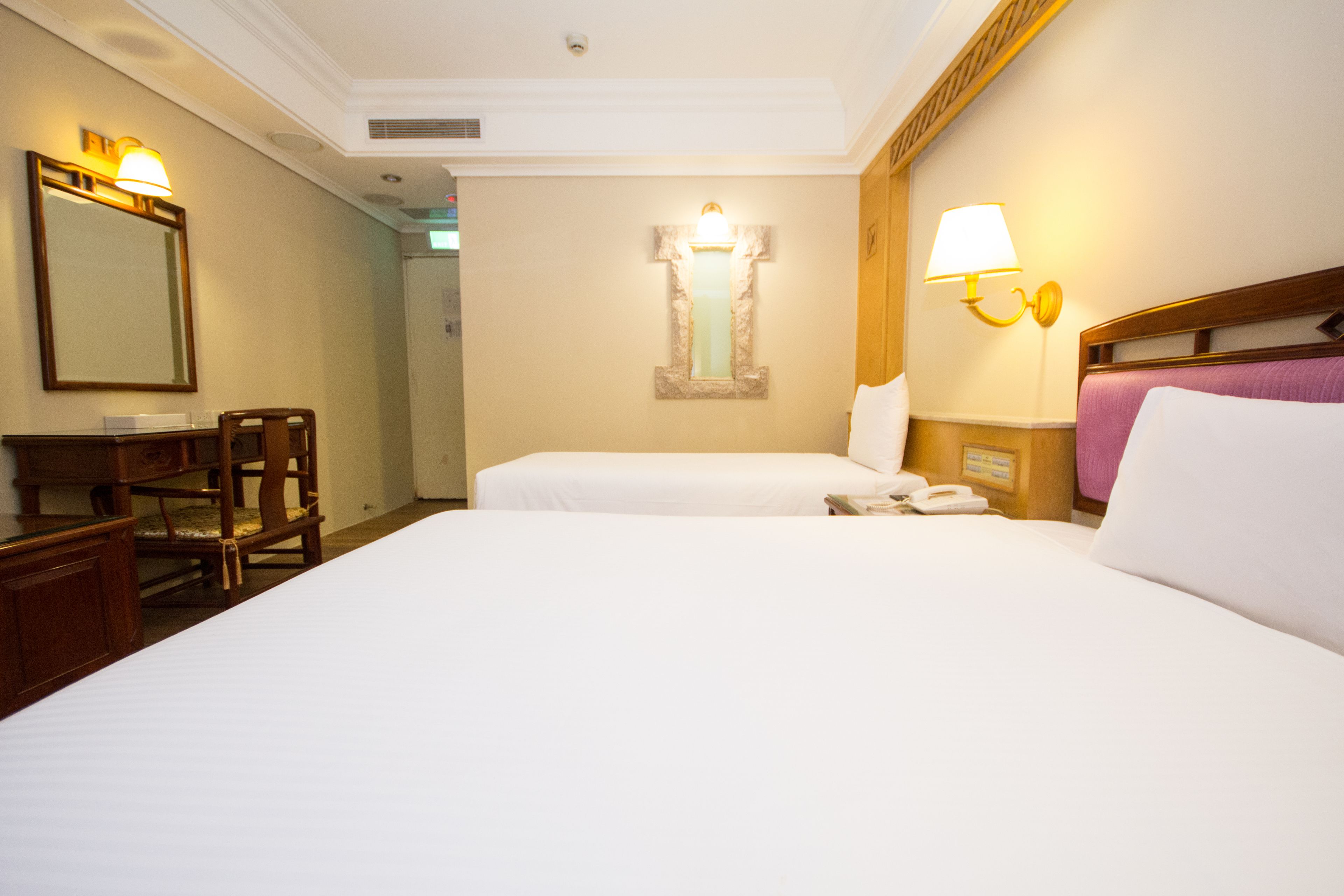 Une chambre d’hôtel avec deux lits, un bureau, une chaise et un miroir.