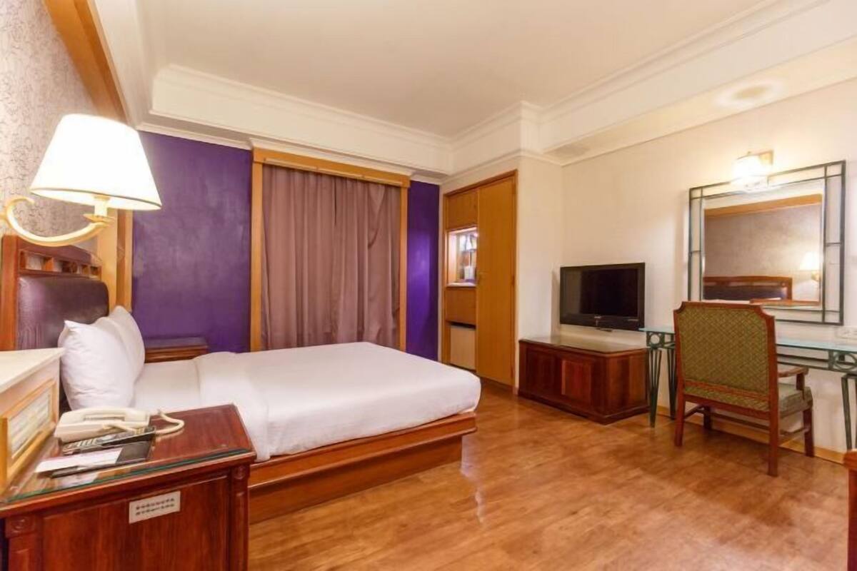 A hotel room with a bed, a television, a desk with a telephone, and a chair.