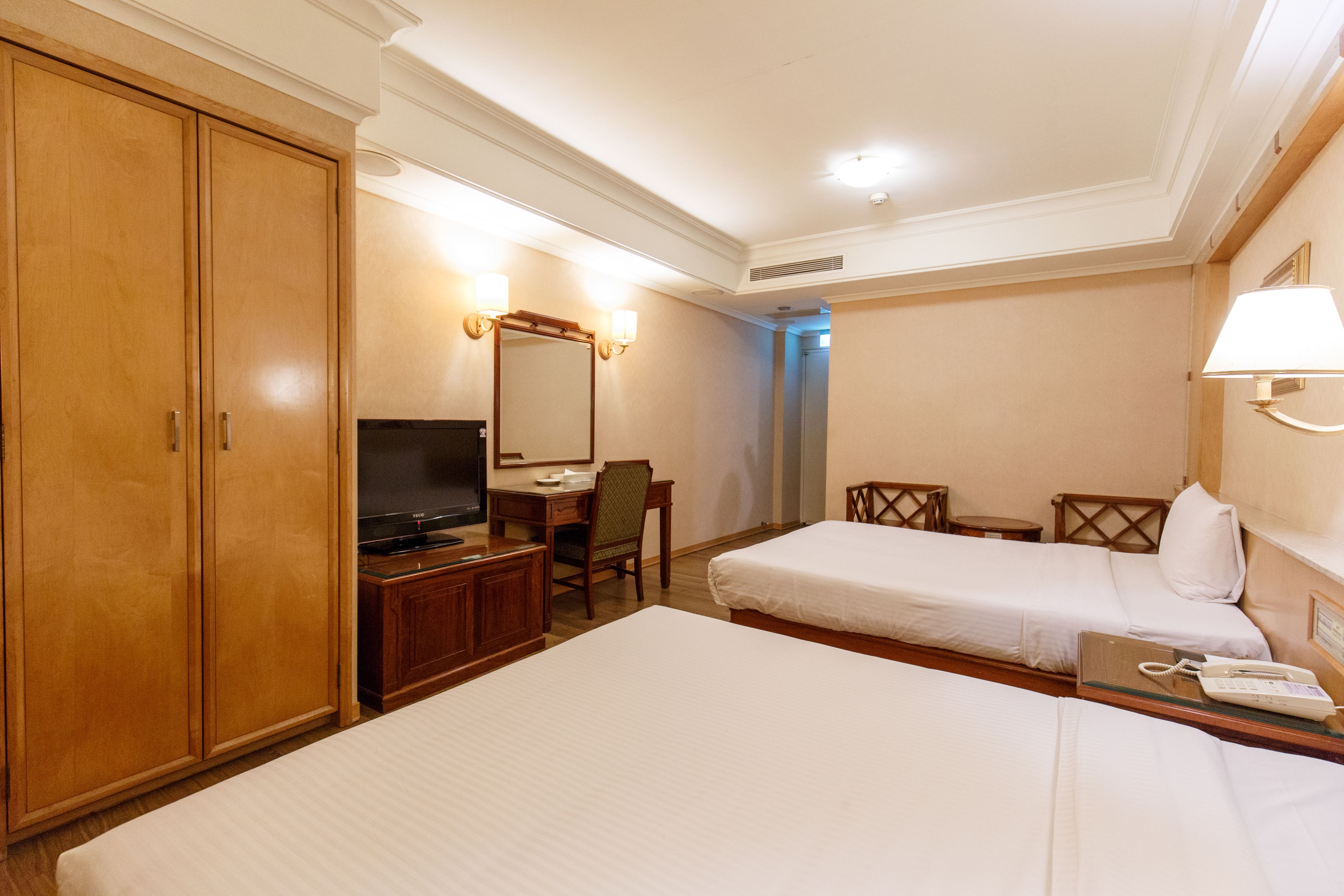 A hotel room with two single beds, a desk with a chair, a television, and a wardrobe.