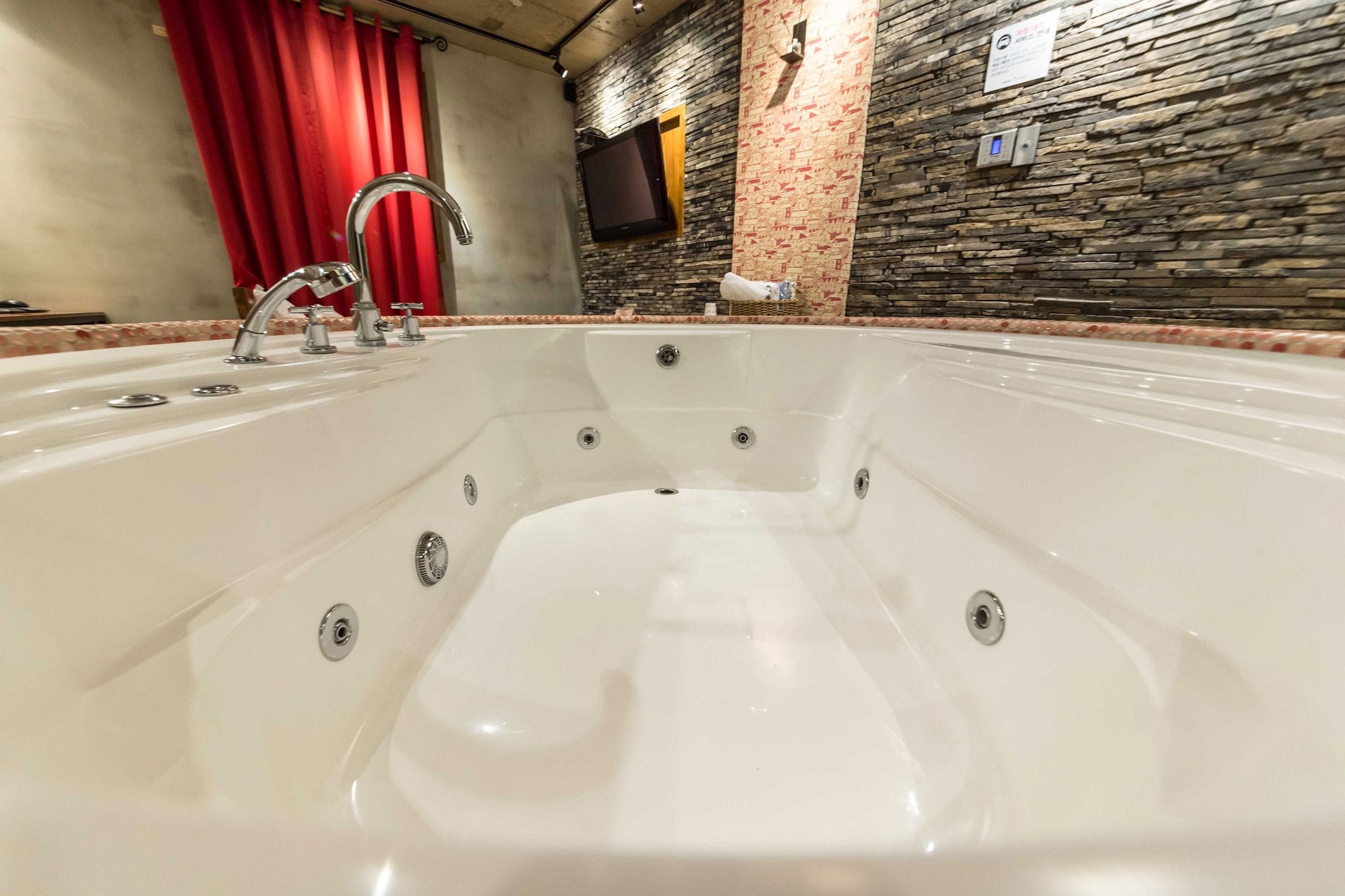 A large, white bathtub with multiple faucets and a stone wall backdrop.