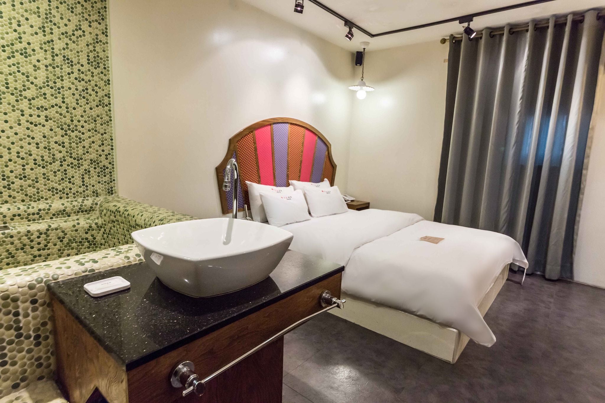 A hotel room with a large bed, a bedside table with a white sink, and a patterned wall.
