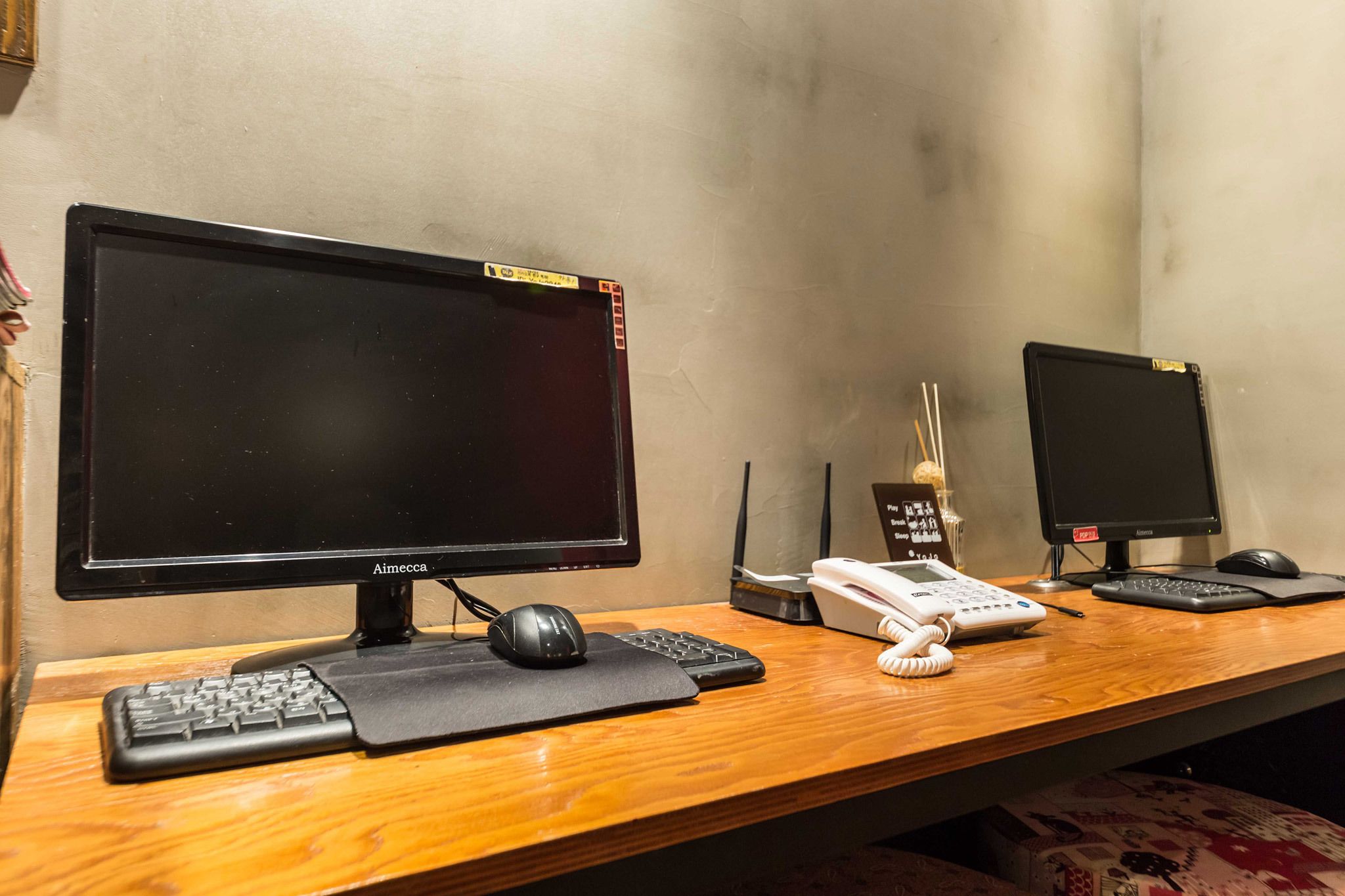Two black monitors on a wooden desk with a keyboard, mouse, and telephone.