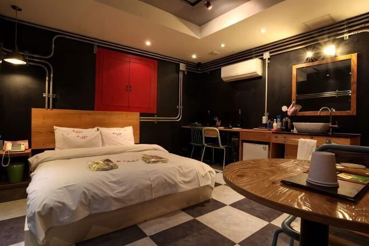 A hotel room with a bed, a desk, a chair, a sink, and a mirror.