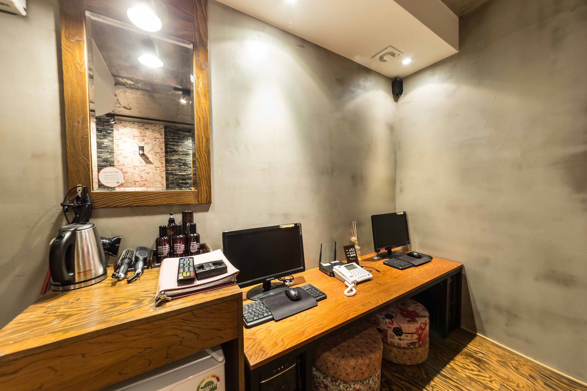 A wooden desk with two monitors, a keyboard, a mouse, a telephone, and a coffee maker.