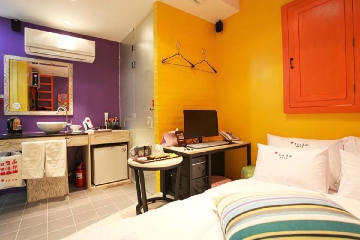 Une chambre d’hôtel comprenant un lit, un bureau, une chaise, une petite table, un miroir, un lavabo et une armoire.