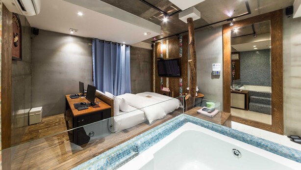 A modern hotel room with a glass-enclosed desk, a bed with a white mattress, a large bathtub, and a wooden vanity with a mirror. - Hotel Yaja Yeongdeungpo (Seoul)