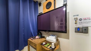A room with a large TV, a small desk with toiletries, a blue curtain, and a sign indicating a car rental service. - Hotel Yaja Yeongdeungpo (Seoul)