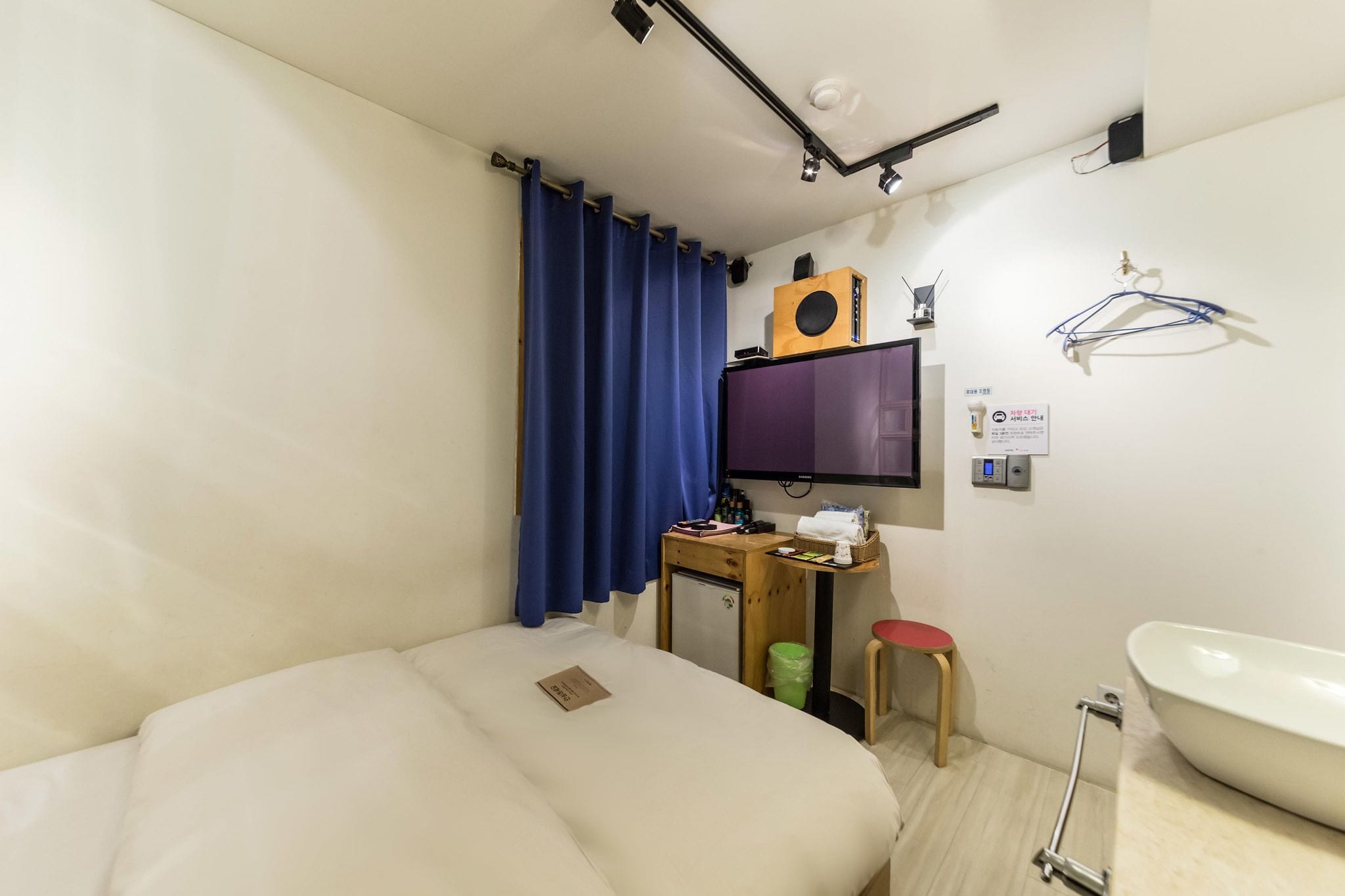 A compact hotel room with a bed, a desk with a computer, a small fridge, a toilet, and a bathtub.
