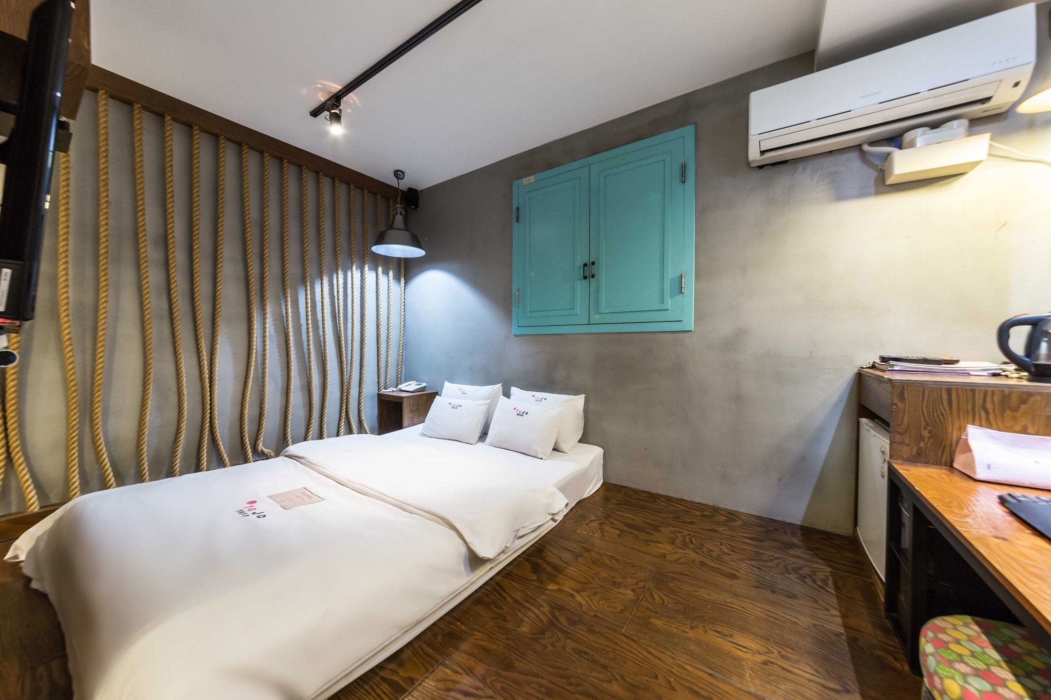 A hotel room with a bed, a desk, an air conditioning unit, and a wardrobe.