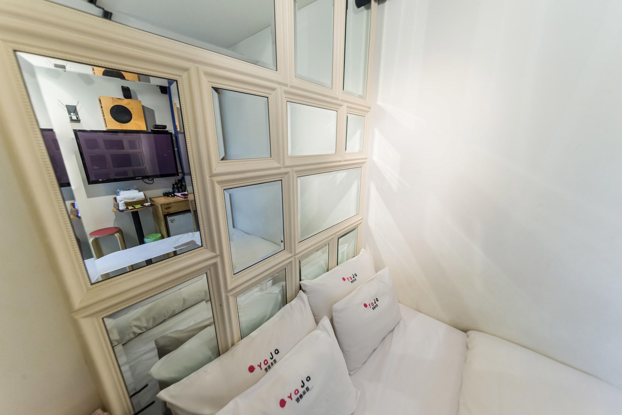 Habitación de hotel con cama, espejo, televisión y ventana con vista al interior de la habitación.