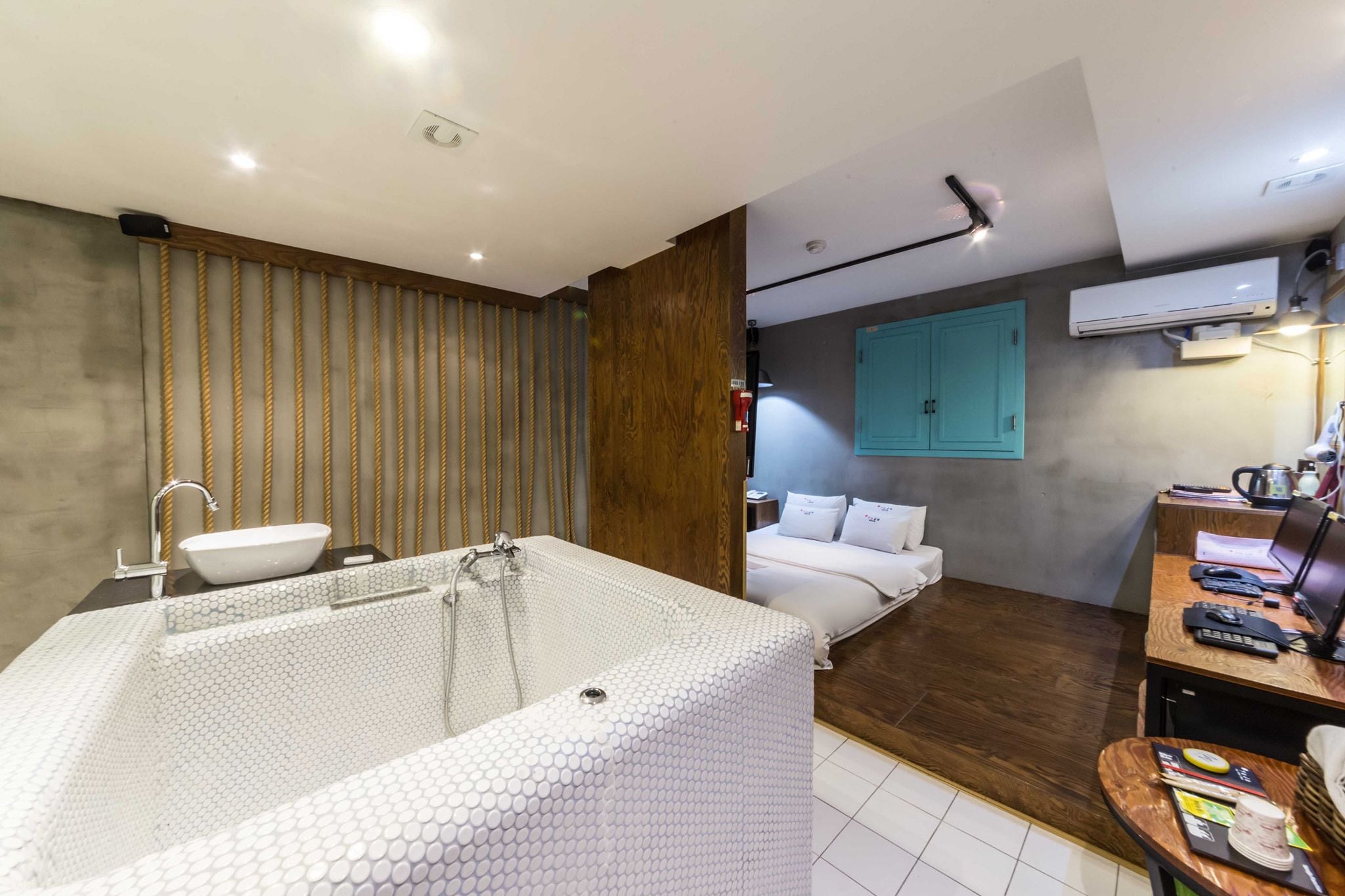 A modern bathroom with a large bathtub, a wooden panel wall, and a bed with white bedding.