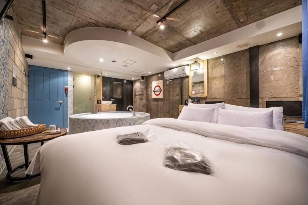 A hotel room with a large bed, a bathroom with a bathtub, a phone on a table, and a blue door.