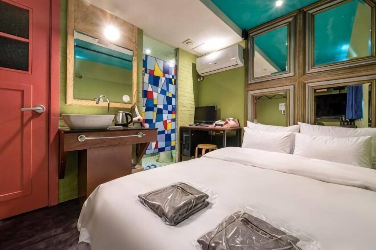A hotel room with a bed, a sink, a mirror, a television, and a window.