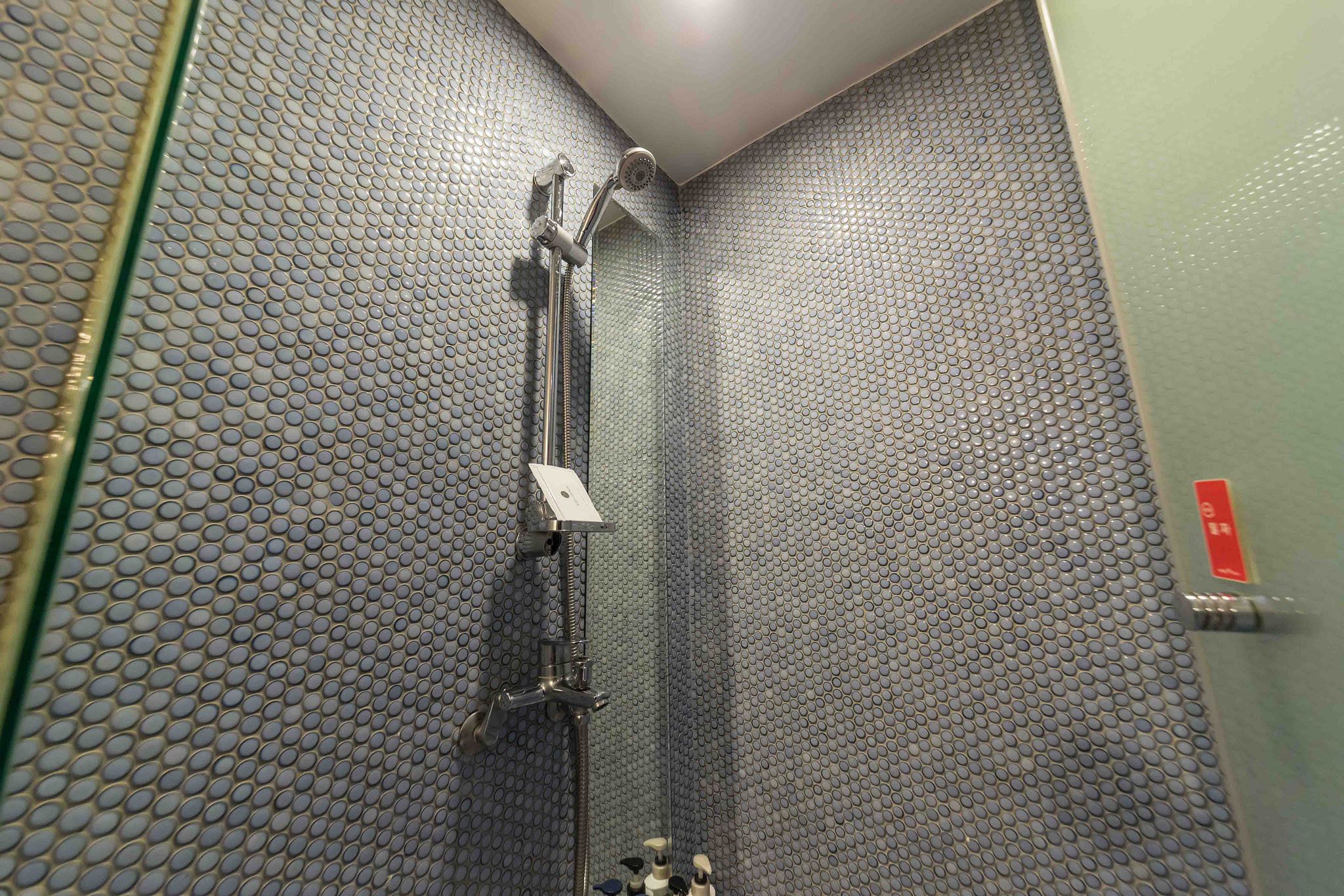 A shower with a perforated wall and a handheld showerhead.