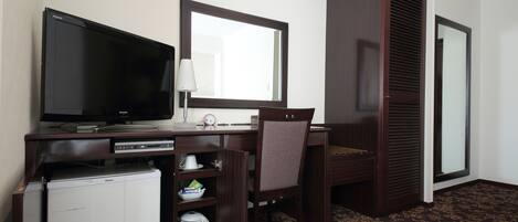 Habitación de hotel con televisión de pantalla plana, escritorio con lámpara, silla, refrigerador pequeño y microondas.