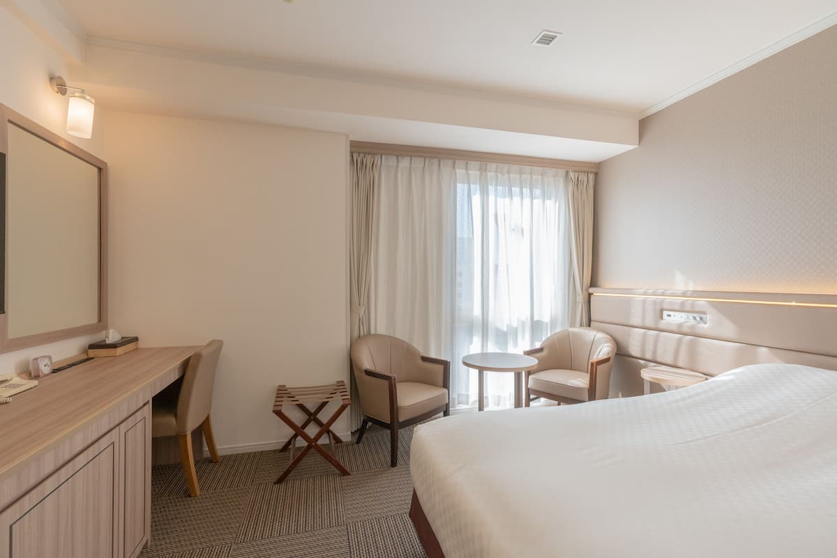 A hotel room with a bed, a desk, two chairs, a small table, and a large mirror.