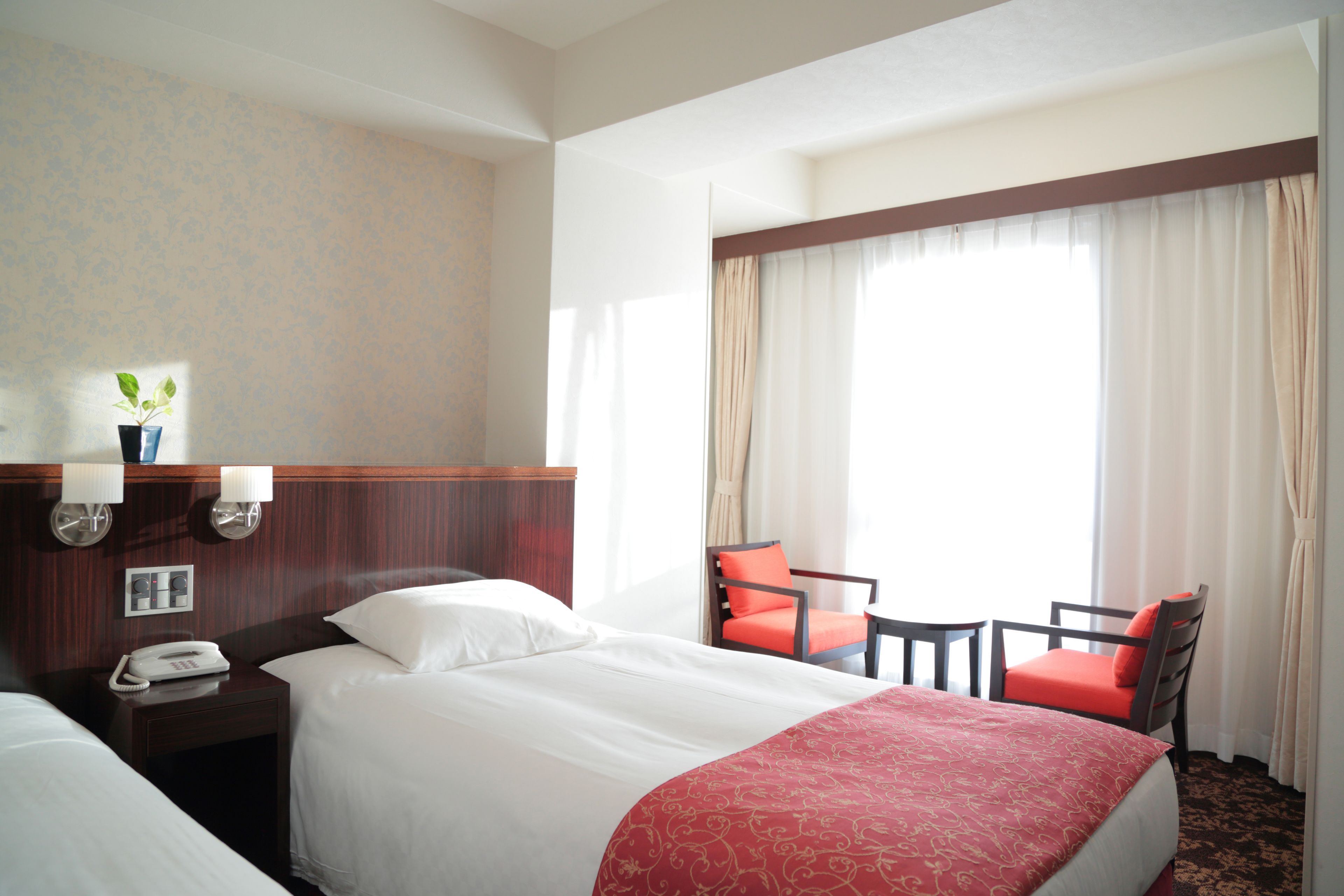 Una habitación de hotel con una cama grande, un escritorio con teléfono, dos sillas y una ventana con cortinas.