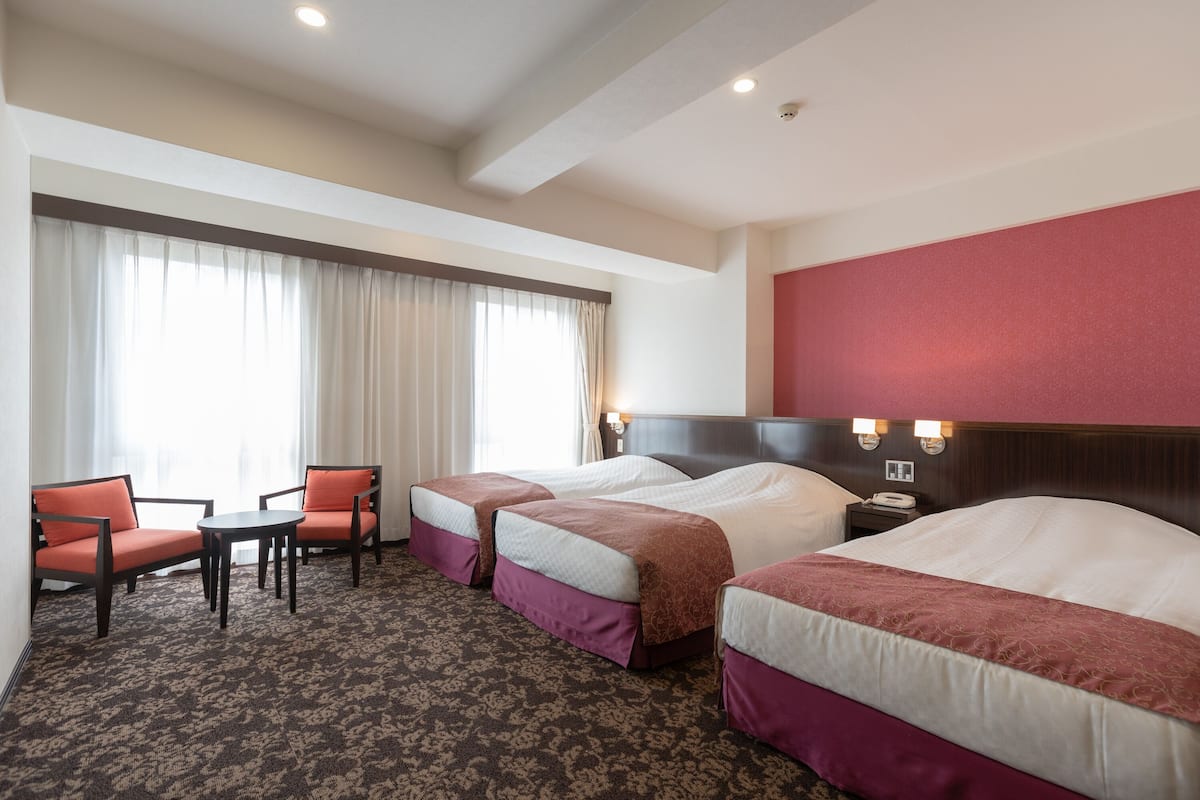 A hotel room with two beds, a desk, chairs, and a large window with curtains.