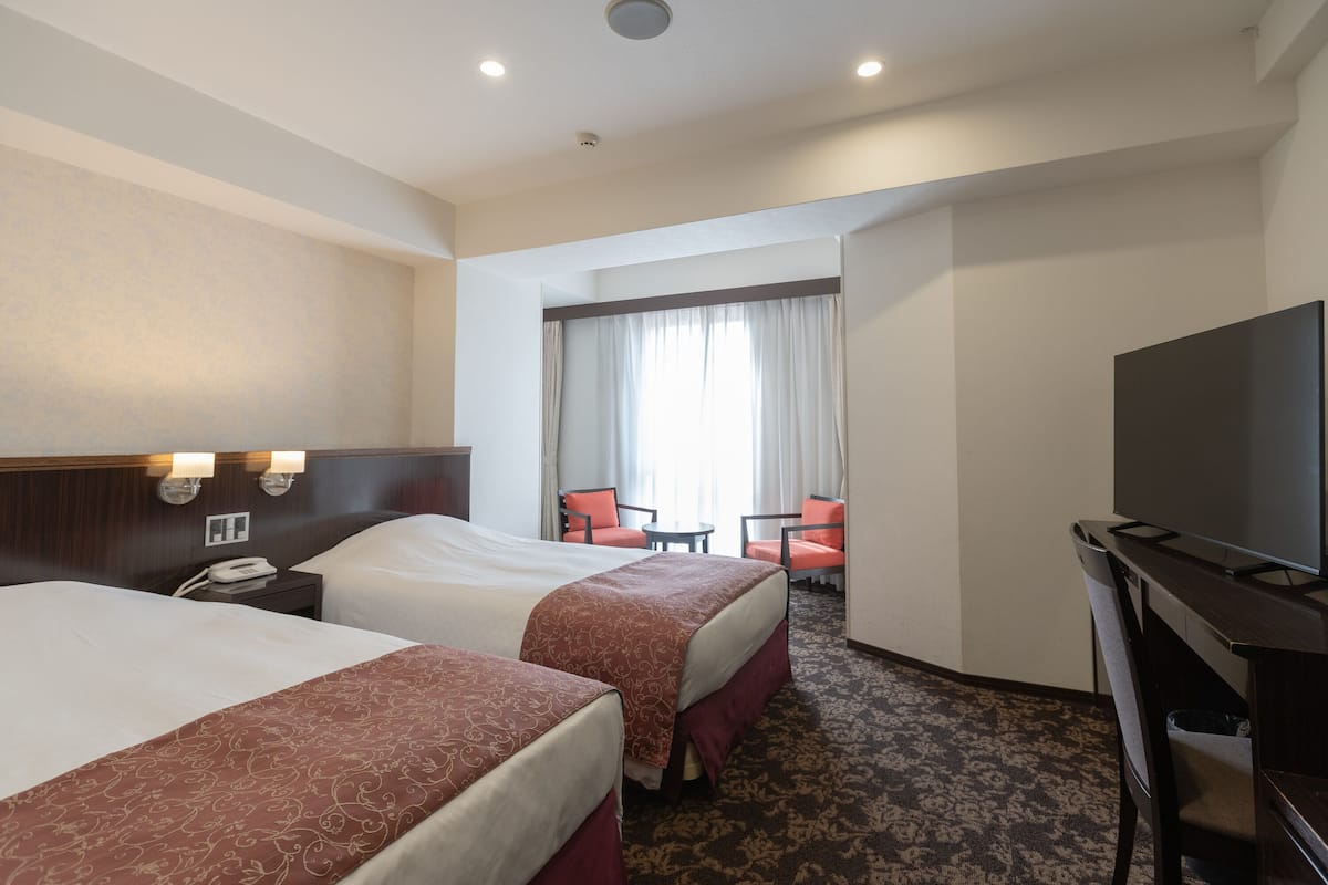 A hotel room with two beds, a TV, a desk, and a chair.