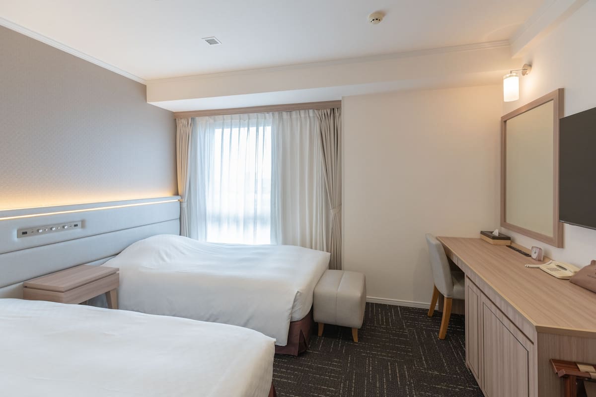 A hotel room with two beds, a desk, a chair, a large mirror, and a window with curtains.