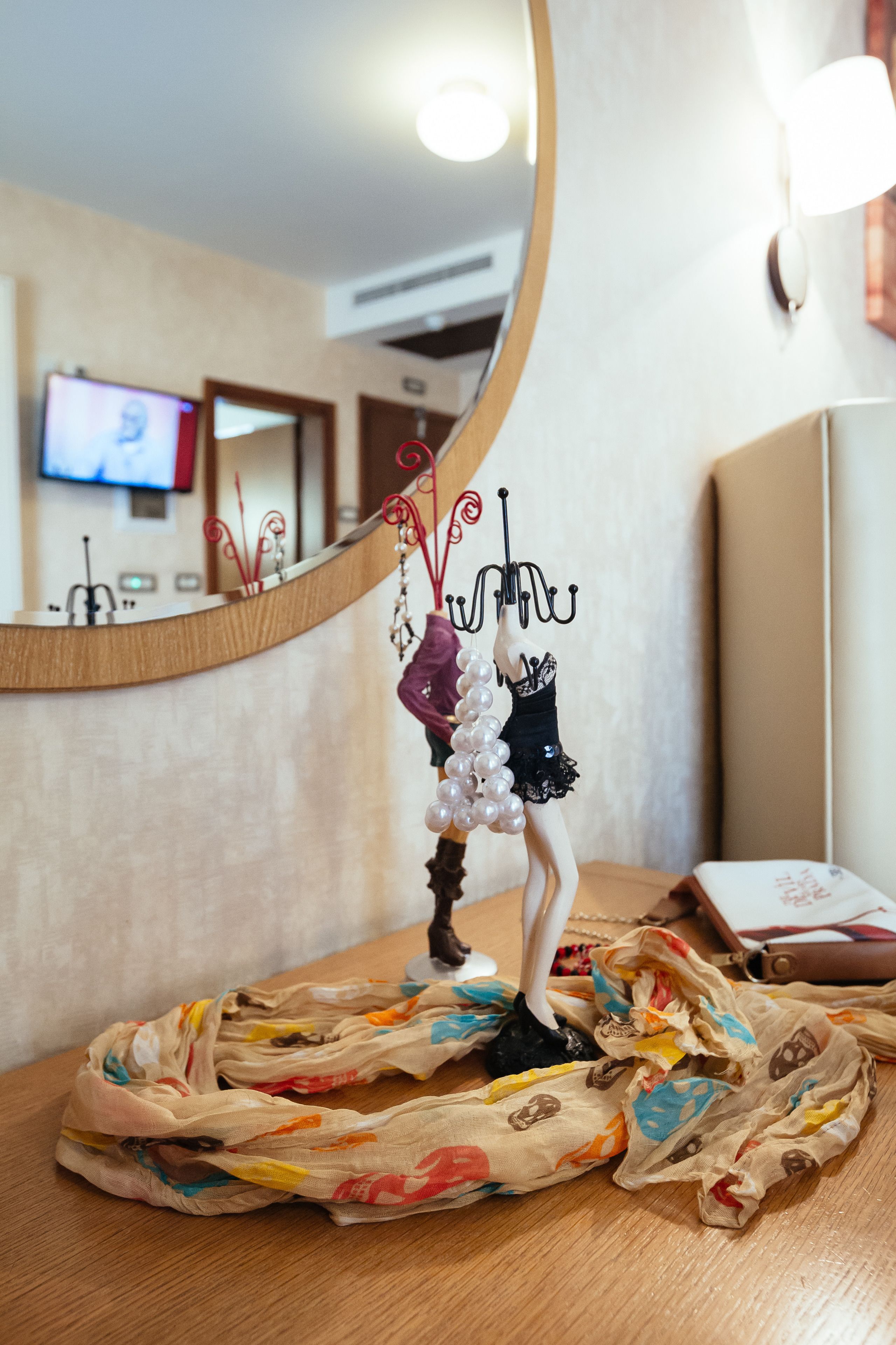 Un espace d’accueil d’hôtel avec un miroir incurvé, un téléviseur et une figurine décorative posée sur une table.