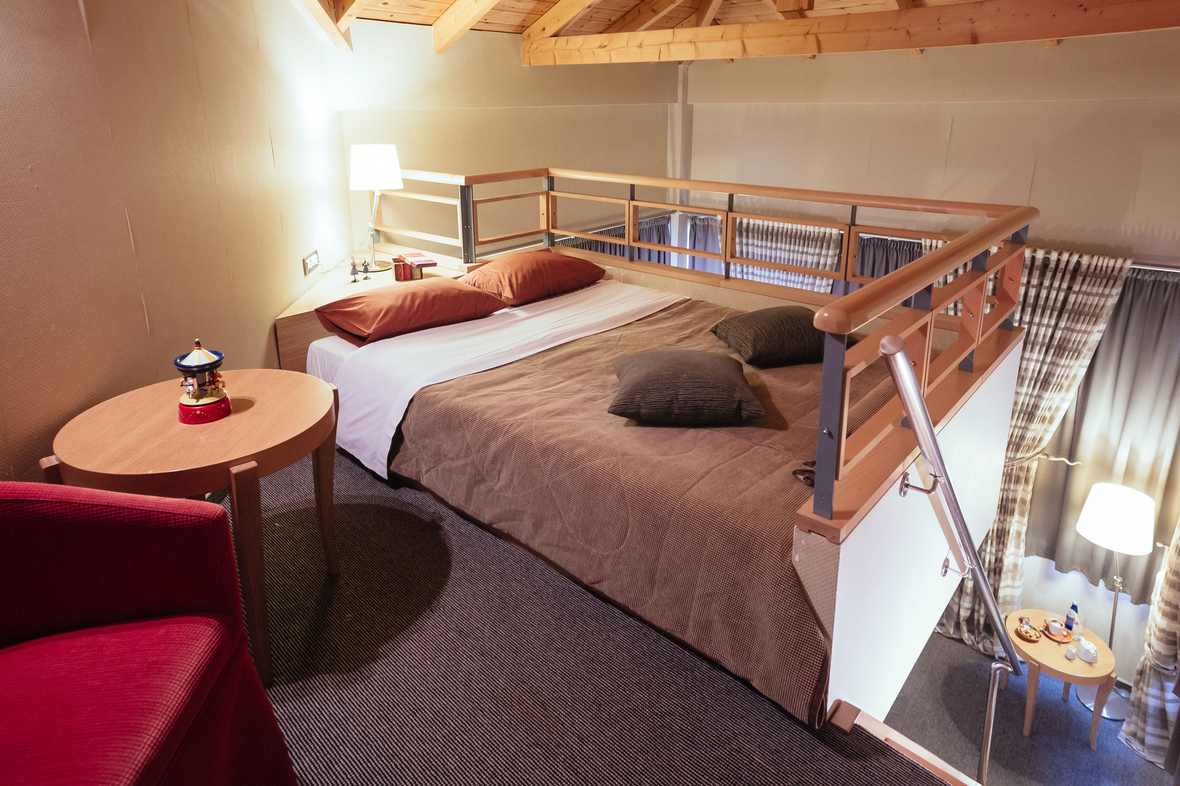 Una habitación acogedora con una cama litera, una mesita redonda con una lámpara y una silla roja.
