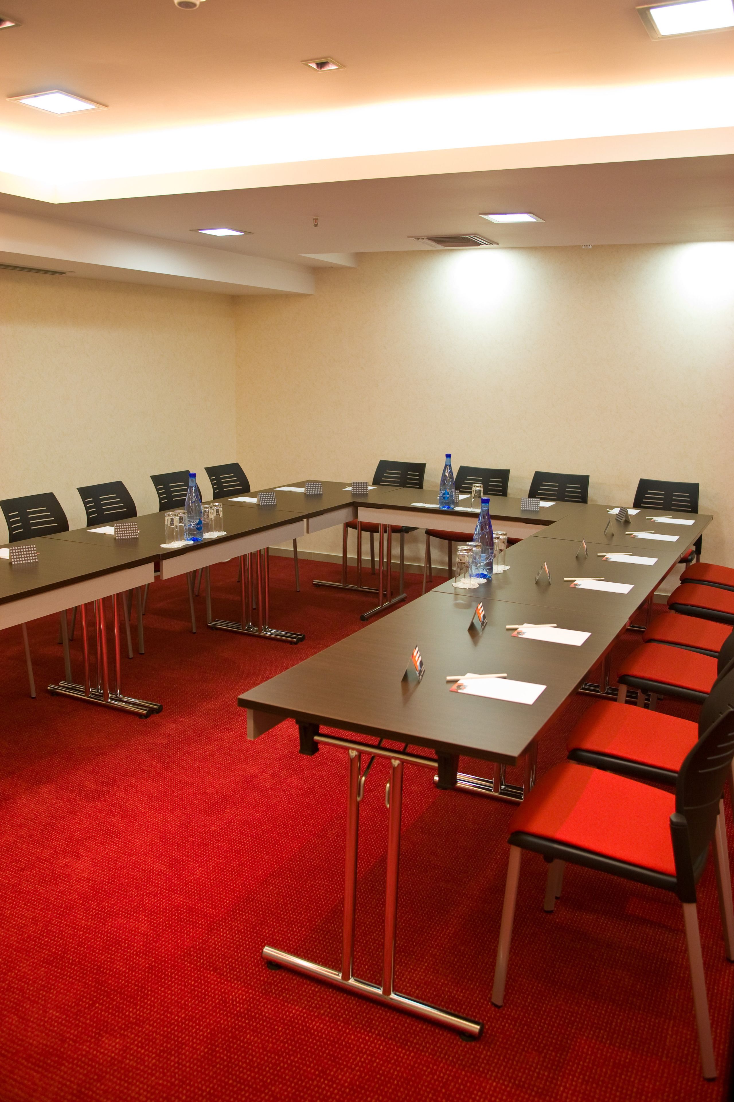 Een vergaderzaal met een lange tafel, stoelen en een rood tapijt.